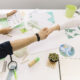 Two people shaking hands over a desk with business and environmental documents.