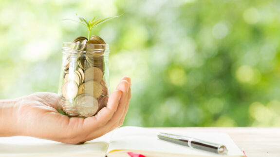 Woman hand holding plant growing from coins bottle Woman hand holding plant growing from coins bottle in the on blurred green natural background